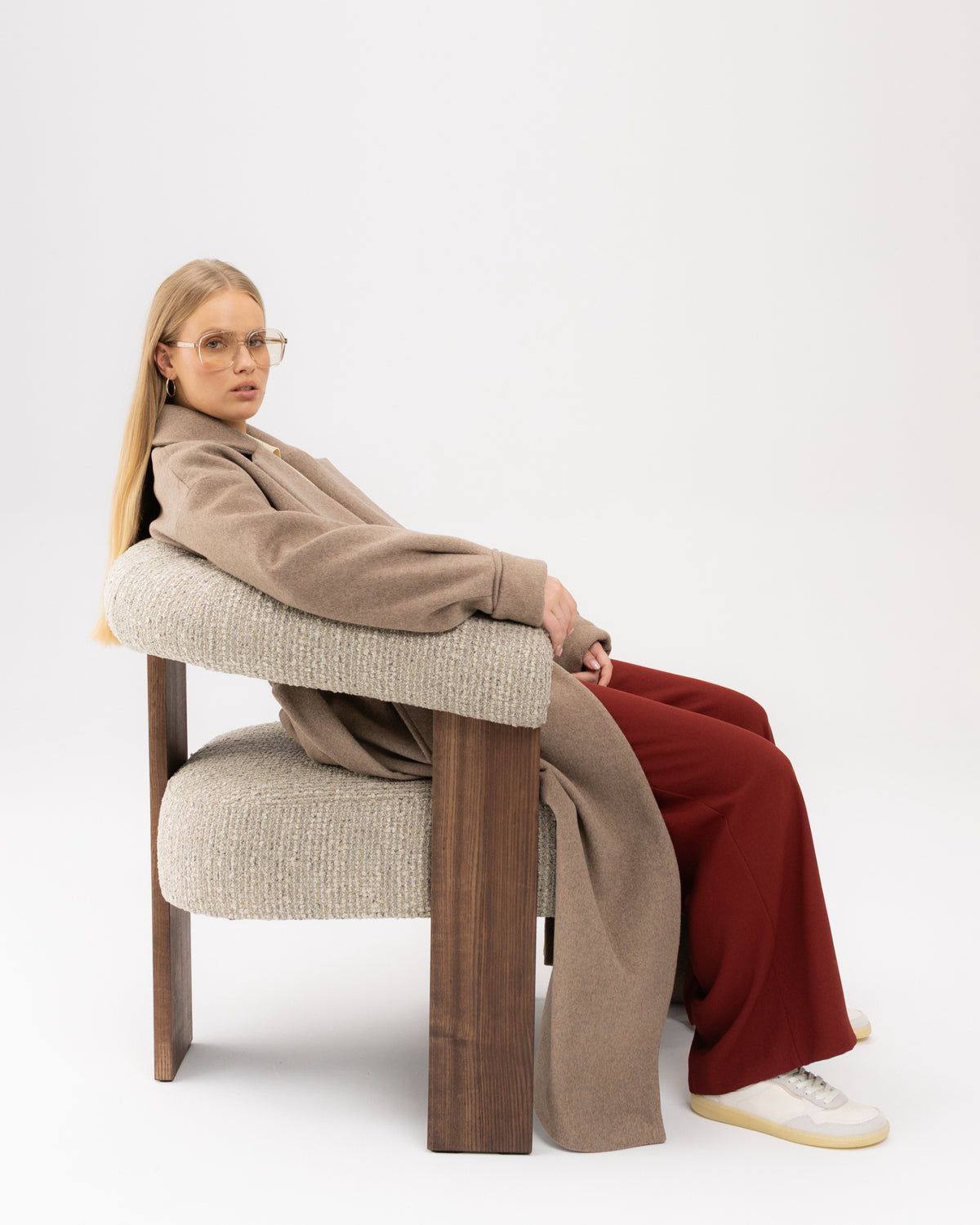 Beżowy płaszcz oversize mokka na modelce siedzącej w fotelu
