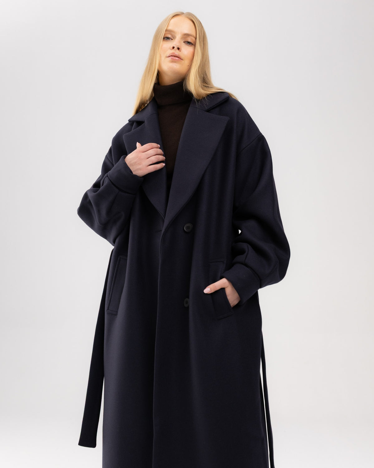 Rozpięty granatowy wełniany płaszcz oversize na modelce z ręką w kieszeni, ujęcie do kolan