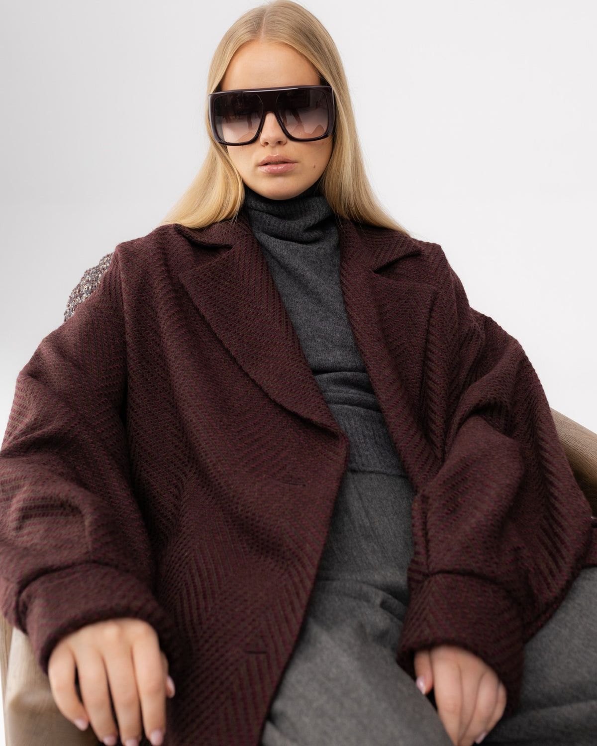 Płaszcz oversize w bordową jodełkę na siedzącej modelce