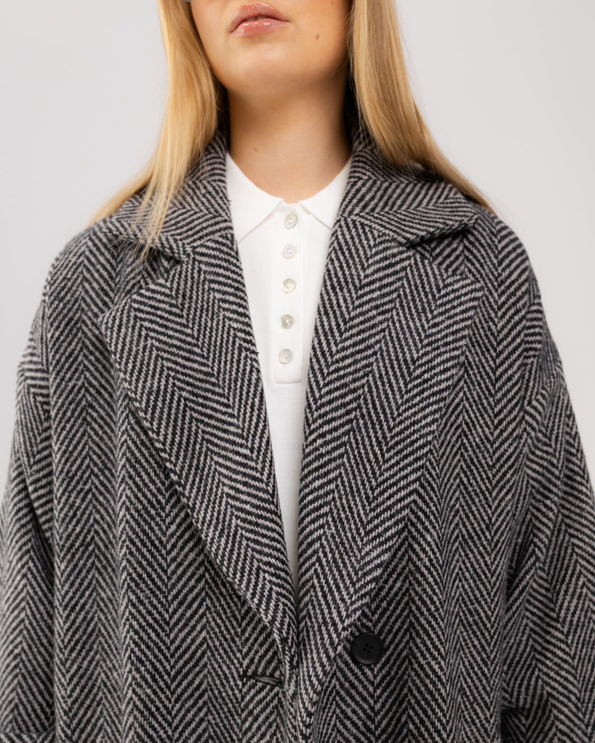 Płaszcz oversize w czarno-białą jodełkę na modelce, ujęcie do pasa