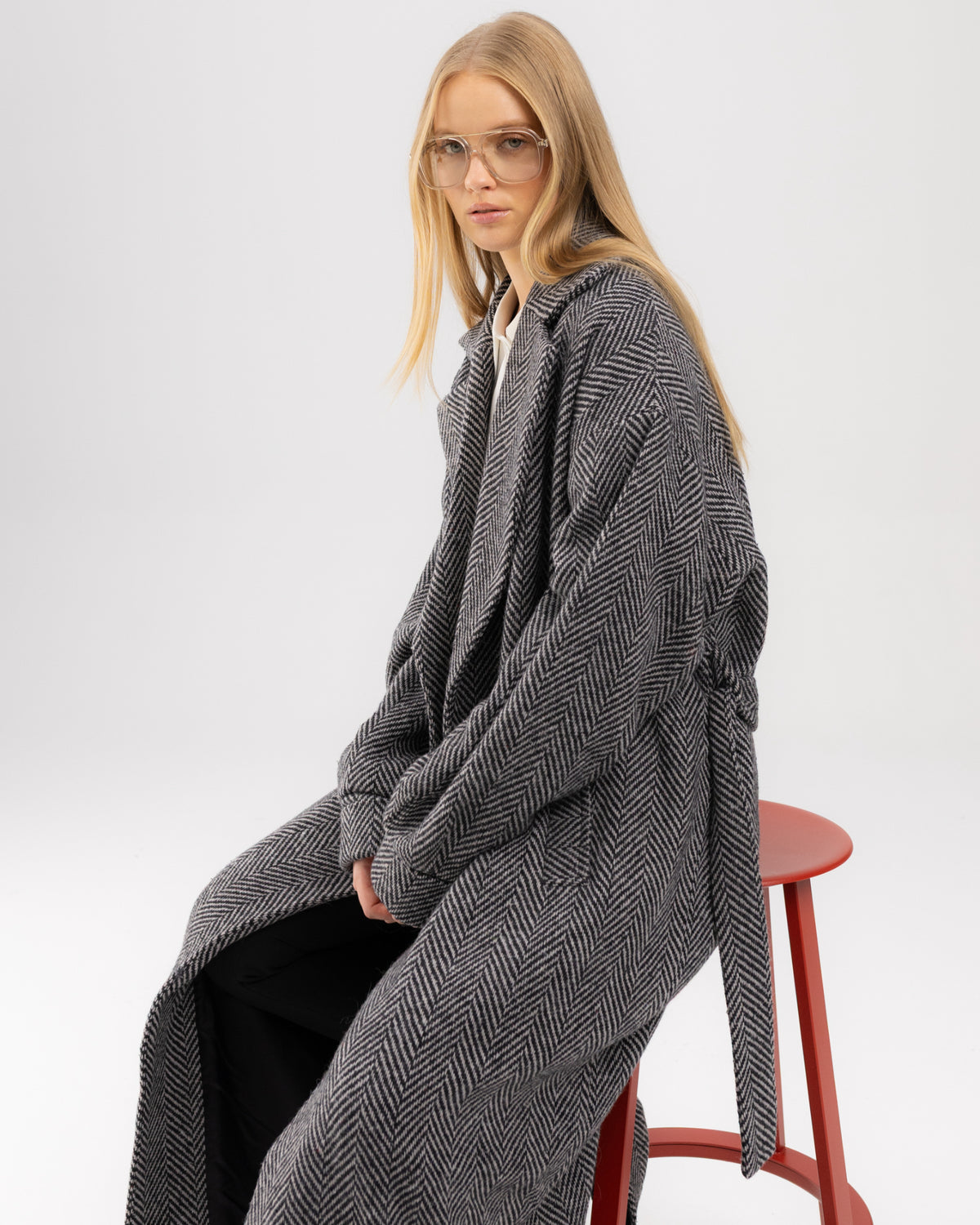 Płaszcz oversize w czarno-białą jodełkę na modelce siedzącej na stołku